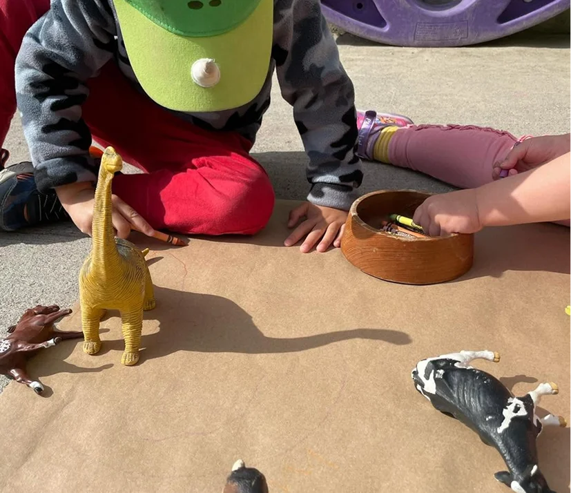 Children drawing outdoors with dinosaur and farm animal toys at Learning Together Childcare